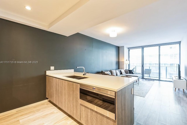 kitchen with kitchen peninsula, floor to ceiling windows, sink, and light wood-type flooring