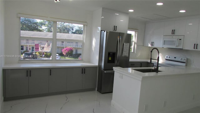 kitchen with stove, sink, decorative backsplash, stainless steel fridge, and white cabinetry