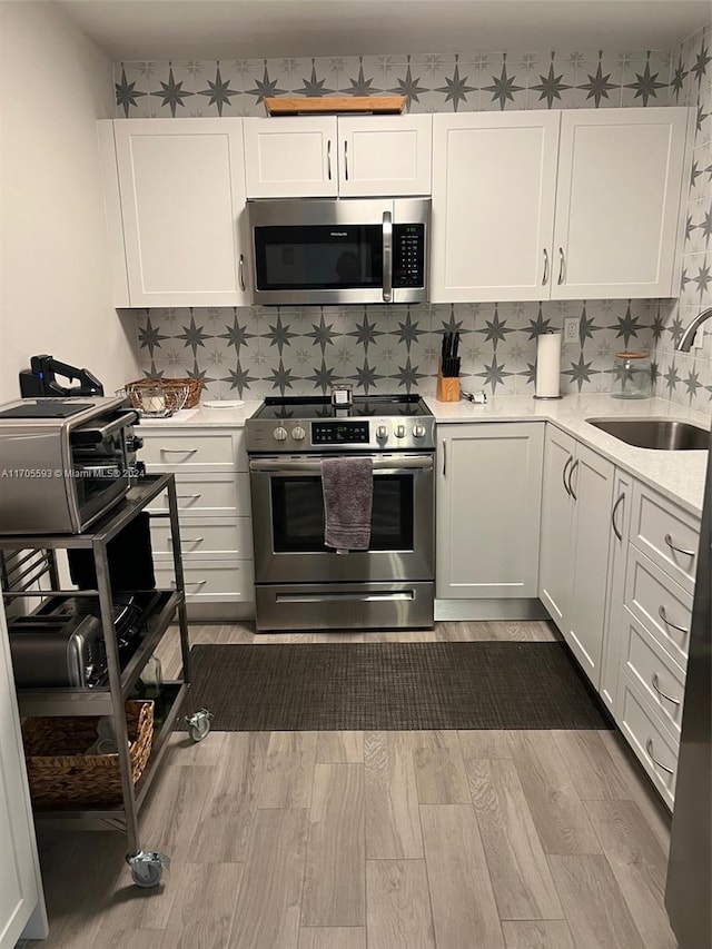 kitchen with sink, stainless steel appliances, tasteful backsplash, white cabinets, and hardwood / wood-style flooring