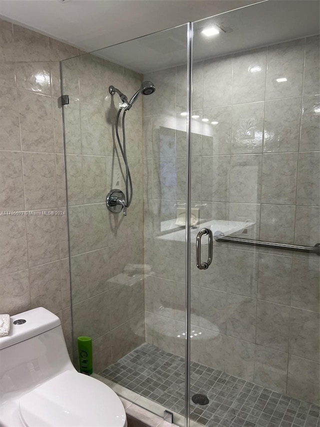 bathroom featuring toilet, an enclosed shower, and tile walls