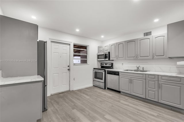 kitchen featuring appliances with stainless steel finishes, light wood-type flooring, light stone counters, sink, and gray cabinets