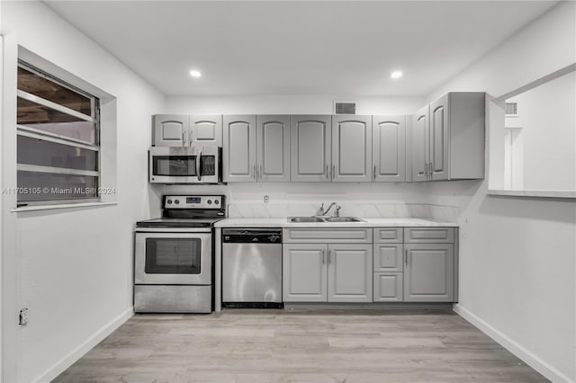 kitchen featuring appliances with stainless steel finishes, light hardwood / wood-style flooring, gray cabinetry, and sink