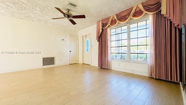 spare room with a wealth of natural light, ceiling fan, a textured ceiling, and light wood-type flooring