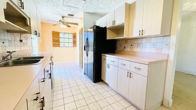 kitchen with decorative backsplash, black fridge with ice dispenser, a textured ceiling, sink, and white cabinets