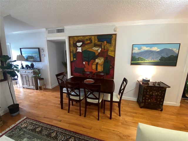 dining area with ornamental molding, a textured ceiling, and light wood-type flooring