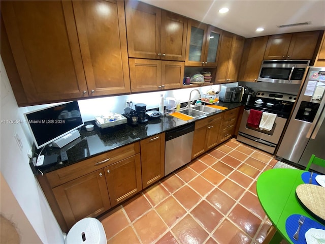 kitchen featuring dark stone counters, sink, light tile patterned floors, and stainless steel appliances