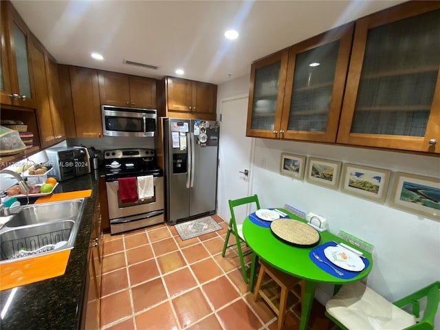 kitchen featuring dark stone counters, sink, light tile patterned flooring, and stainless steel appliances