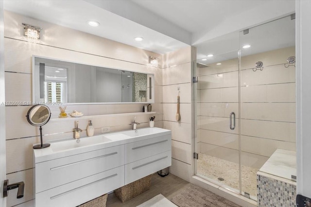 full bathroom with double vanity, a stall shower, a sink, and tile walls