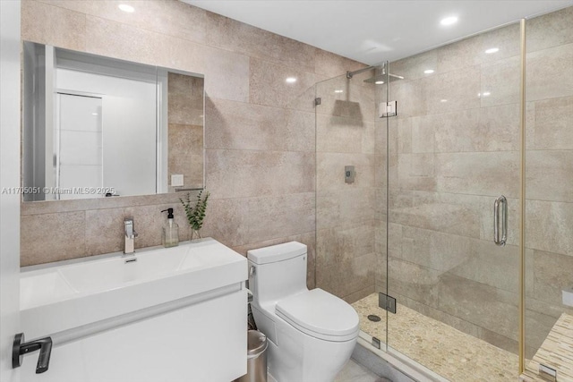 bathroom with toilet, vanity, tile walls, a shower stall, and tasteful backsplash