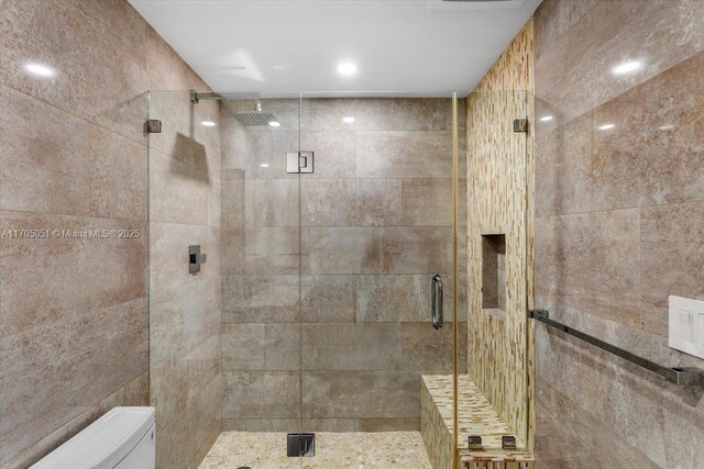 bathroom with a shower with door, tile walls, and toilet