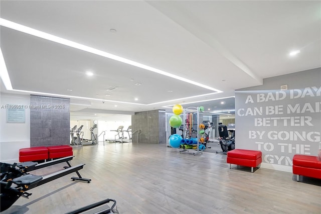 workout area with a tray ceiling and light wood-style flooring