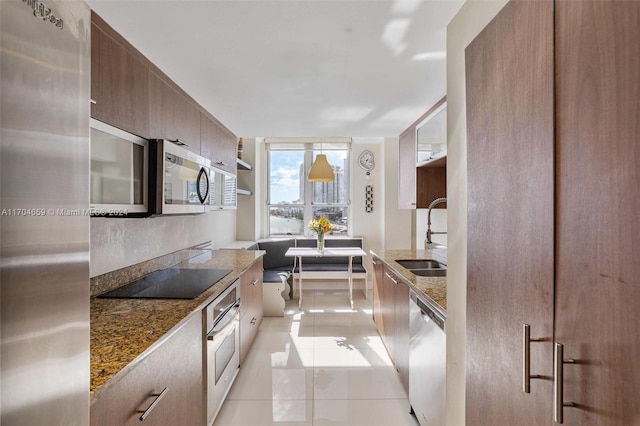 kitchen with light tile patterned floors, stainless steel appliances, dark stone counters, and sink