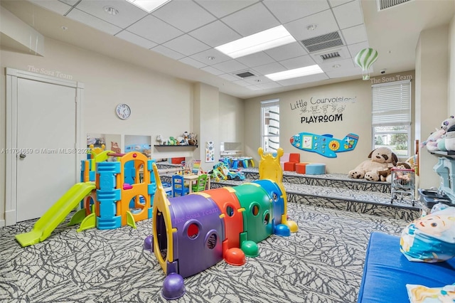 rec room with carpet floors, a drop ceiling, and a healthy amount of sunlight