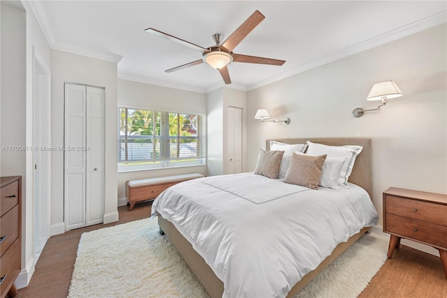 bedroom featuring ceiling fan, hardwood / wood-style floors, crown molding, and two closets