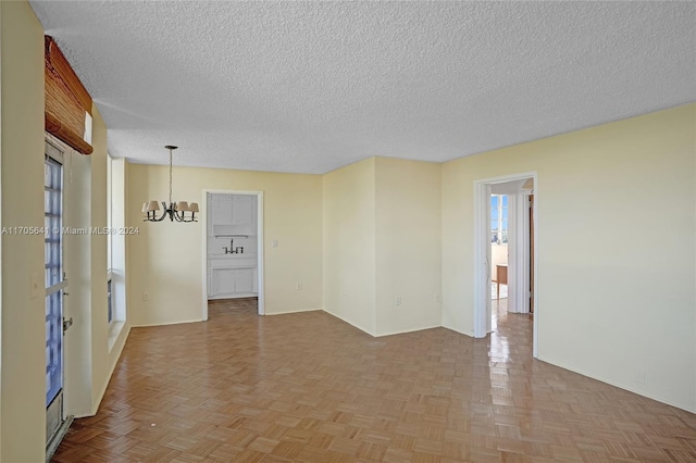 empty room with sink, light parquet flooring, a textured ceiling, and a notable chandelier