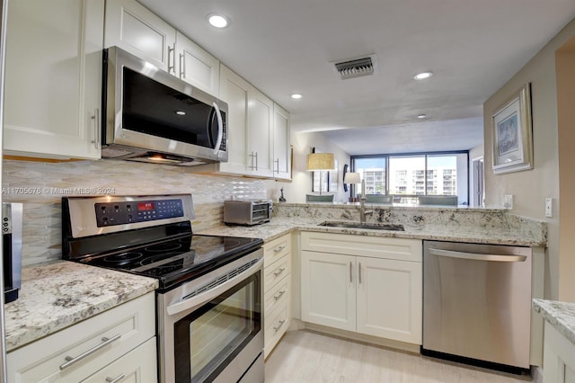 kitchen featuring white cabinets, sink, light stone countertops, tasteful backsplash, and stainless steel appliances