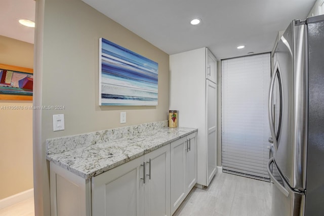 kitchen with white cabinetry, stainless steel fridge, and light stone counters