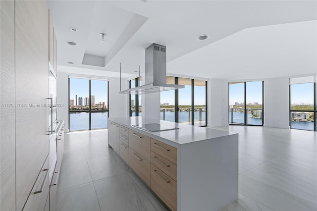 kitchen featuring expansive windows, island range hood, black electric cooktop, a water view, and a large island