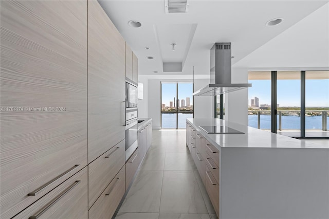 interior space featuring light brown cabinetry, black electric stovetop, island range hood, a water view, and stainless steel microwave