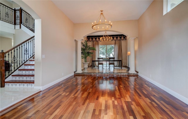 unfurnished dining area with arched walkways, a notable chandelier, wood finished floors, baseboards, and decorative columns