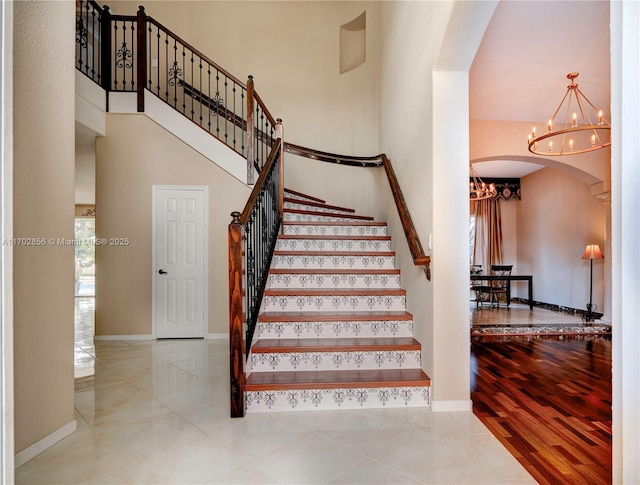 staircase featuring arched walkways, a high ceiling, an inviting chandelier, wood finished floors, and baseboards