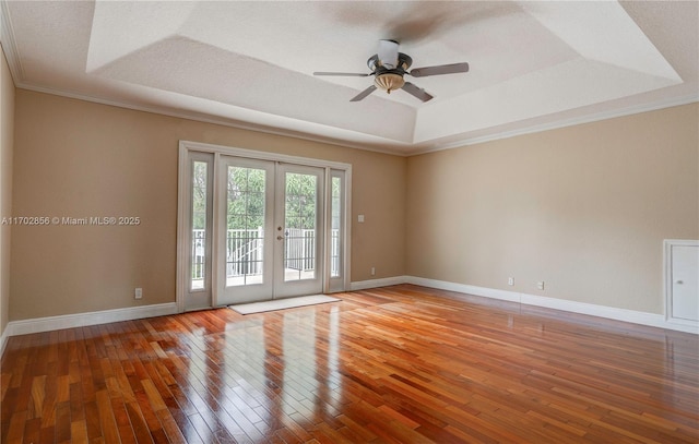 spare room with french doors, a tray ceiling, wood finished floors, and baseboards