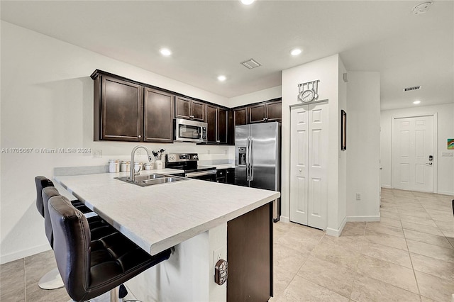 kitchen featuring a kitchen bar, appliances with stainless steel finishes, kitchen peninsula, dark brown cabinetry, and sink