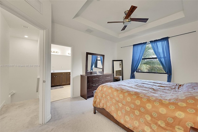 carpeted bedroom with ceiling fan, ensuite bath, and a tray ceiling