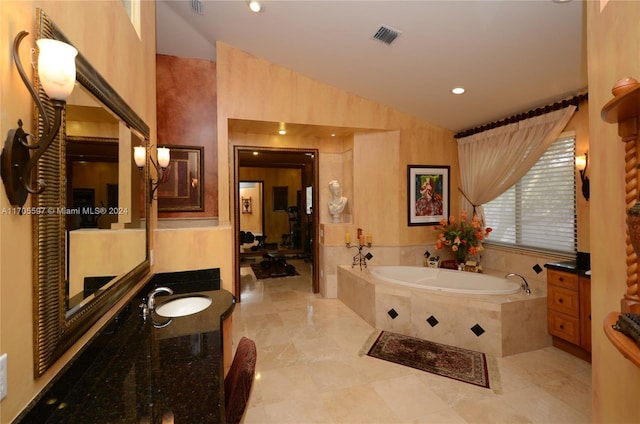 bathroom featuring tiled tub, vanity, and vaulted ceiling