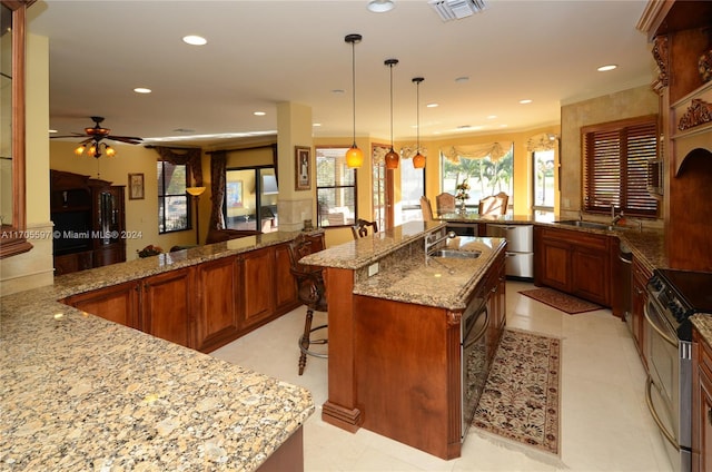 kitchen featuring kitchen peninsula, light stone counters, stainless steel range, a spacious island, and pendant lighting