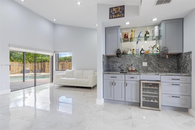 bar featuring gray cabinetry, decorative backsplash, dark stone countertops, and wine cooler