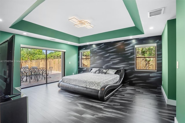 bedroom with access to outside, a raised ceiling, and hardwood / wood-style floors