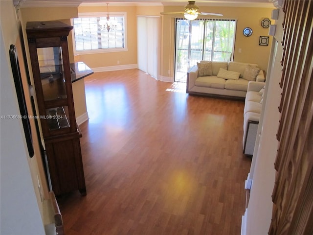 living room with ceiling fan with notable chandelier, a healthy amount of sunlight, wood-type flooring, and crown molding