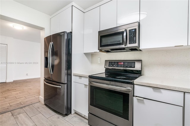 kitchen featuring appliances with stainless steel finishes, light wood-type flooring, tasteful backsplash, and white cabinetry