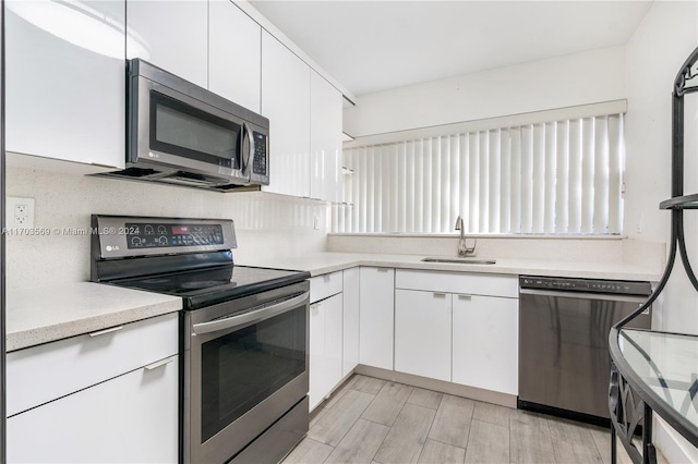 kitchen featuring sink, decorative backsplash, light wood-type flooring, appliances with stainless steel finishes, and white cabinetry