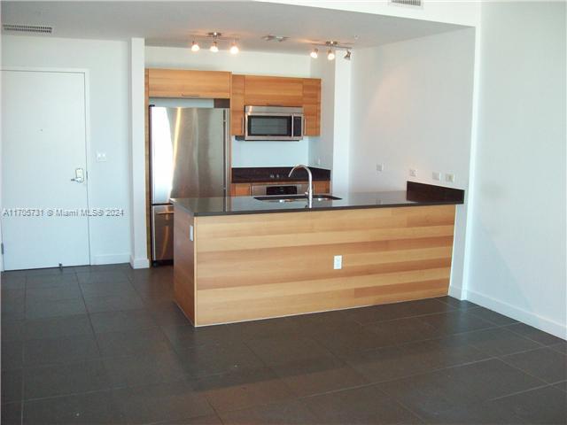 kitchen featuring kitchen peninsula, sink, dark tile patterned floors, and appliances with stainless steel finishes