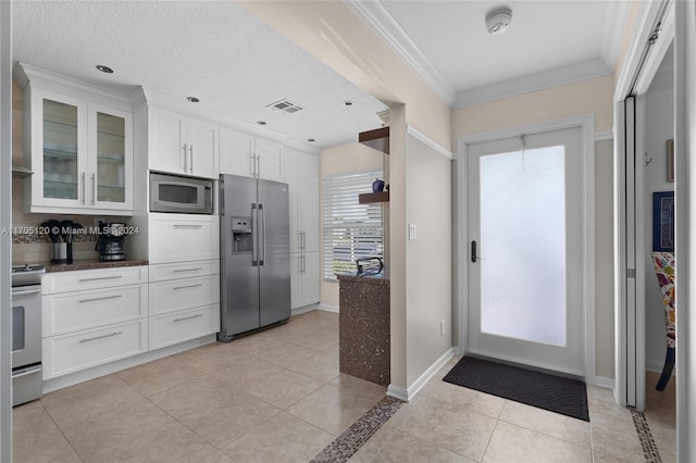 kitchen with appliances with stainless steel finishes, a textured ceiling, crown molding, light tile patterned floors, and white cabinets