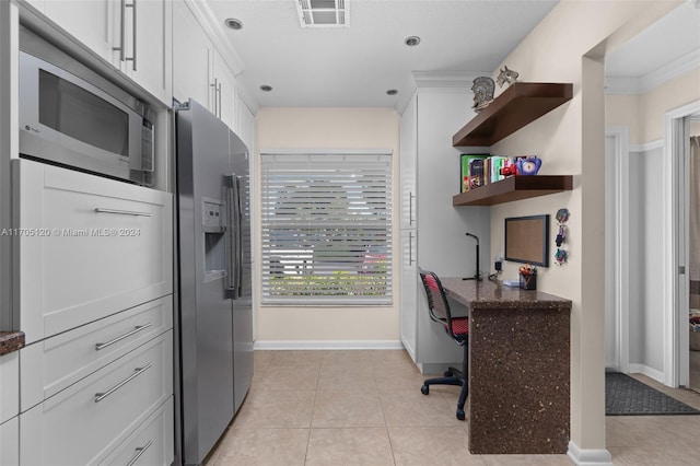 kitchen with white cabinets, ornamental molding, light tile patterned floors, and appliances with stainless steel finishes