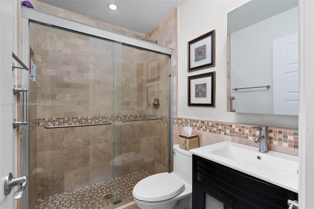 bathroom with vanity, a shower with door, toilet, and tile walls