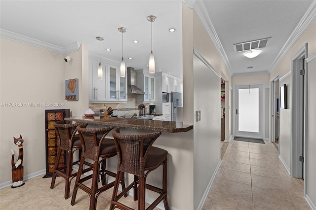 kitchen featuring kitchen peninsula, white cabinets, wall chimney range hood, and ornamental molding