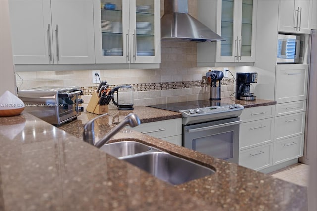 kitchen featuring decorative backsplash, dark stone counters, stainless steel appliances, wall chimney range hood, and white cabinets