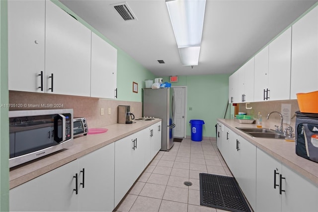 kitchen with sink, tasteful backsplash, light tile patterned flooring, white cabinets, and appliances with stainless steel finishes