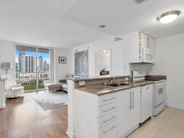 kitchen with white appliances, dark stone counters, sink, light wood-type flooring, and white cabinetry