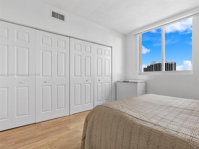 bedroom with light hardwood / wood-style flooring, refrigerator, and a textured ceiling