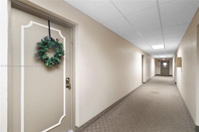 hall with a paneled ceiling and light colored carpet