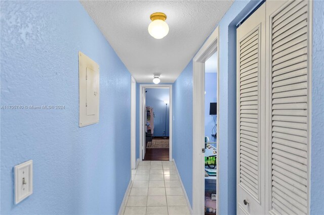 hall with a textured ceiling, electric panel, and light tile patterned flooring