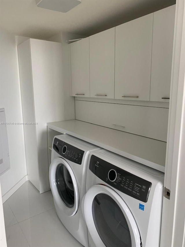 laundry area with washing machine and dryer, light tile patterned floors, and cabinets