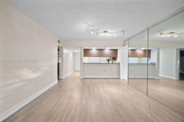 unfurnished living room with track lighting, a textured ceiling, and light hardwood / wood-style flooring