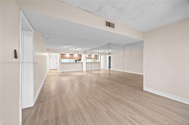 unfurnished living room with track lighting, light hardwood / wood-style floors, and a textured ceiling