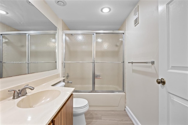 full bathroom with wood-type flooring, vanity, toilet, and bath / shower combo with glass door